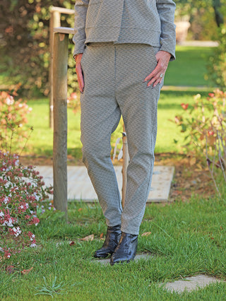 OFF#DLY Pant Lina black/white: Person trägt stilvolle, schmal geschnittene Hose mit feinem, grafischem Muster auf einer Wiese. Kombiniert mit schwarzen Lederstiefeln, bietet sie Komfort durch elastischen Bund.