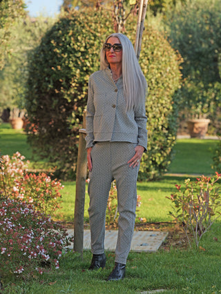 Frau im Garten trägt OFF#DLY Pant Lina black/white, ein elegantes, schmal geschnittenes Outfit mit grafischem Muster und elastischem Bund, kombiniert mit schwarzem Stiefel.