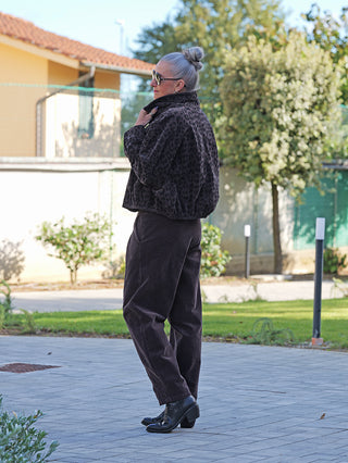 Person trägt OFF#DLY Pant Vada schoko aus weichem Cordmaterial mit lockerem Schnitt und umgeschlagenem Saum, kombiniert mit einer dunklen Jacke und schwarzen Lederstiefeletten.