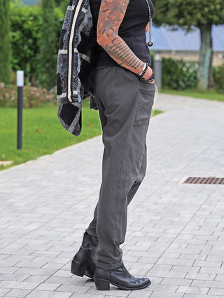 Person trägt OFF#DLY Pant Bora grau, locker sitzende dunkle Hose mit schmal zulaufendem Bein und elastischem Bund, kombiniert mit schwarzen Stiefeletten und einer über die Schulter gelegten karierten Jacke.