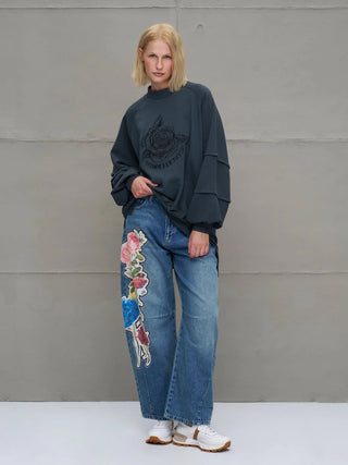 Frau in #VDR Sewatshirt 18156 anthrazit, oversized mit Rundhalsausschnitt und floraler Grafik vorne. Kombiniert mit weiten Jeans und weißen Sneakern.