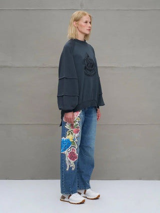 #VDR Sewatshirt 18156 anthrazit, oversized mit floralem Stickmotiv, Rundhalsausschnitt, markante Nahtdetails, lockerer Schnitt, getragen von Frau in Profilansicht mit Jeans und weißen Sneakers.