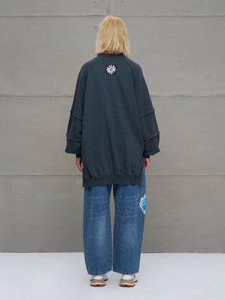 Person von hinten gegen eine Betonwand, trägt #VDR Sewatshirt 18156 anthrazit, oversized mit Rundhalsausschnitt und Nahtdetails, lockere Jeans mit Patch und weiße Schuhe.