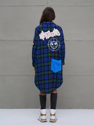 Person trägt #VDR Shirt 18114 royal/black, ein oversized, langes Hemd mit blau-grünem Karomuster, pinker Amazing-Stickerei und blauem Teddy-Fleece-Patch, kombiniert mit weißen Wanderschuhen.