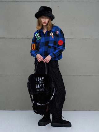 #VDR Shirt 11816 royal/black getragen von einer Frau, kombiniert mit einem schwarzen Rock, Chunky-Sneakern und einem Slogan-Tote. Das Shirt besticht durch Buffalo-Karo und auffällige Patches.