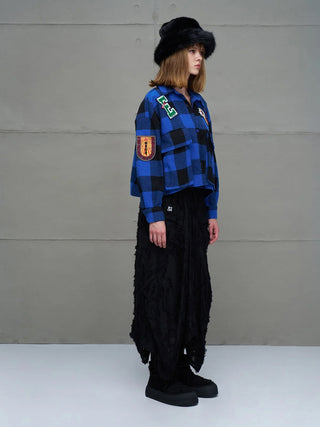 Junge Person trägt das #VDR Shirt 11816 royal/black, ein karierter, oversized Cropped-Shirt mit Patches und Knopfleiste, kombiniert mit einer langen, schwarzen Rock-ähnlichen Kleidung und schwarzen Plateau-Sneakern.