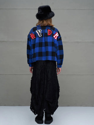 Person von hinten in #VDR Shirt 11816 royal/black: ein kurzes, kariertes Oversized-Hemd mit großen Buchstaben-Patches über den Schultern, kombiniert mit einem schwarzen, plüschigen Hut, langen schwarzen Hosen und Plateauschuhen.