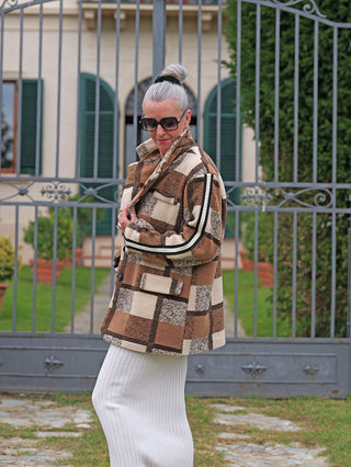 Ältere Frau in OFF#DLY Blazer Grace braun kariert, stilvoll und lässig mit markantem Karomuster, Stehkragen und aufgesetzten Taschen, im Freien vor schmiedeeisernem Tor.