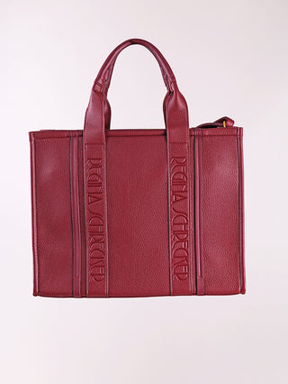 Regina Schrecker Shopper bordeaux aus strukturiertem Kunstleder, mit zwei Lederriemen und vertikalen Markengravuren. Boxiges Design, ideal für stilvolles Tragen, robust und elegant. Perfekt für den täglichen Gebrauch.