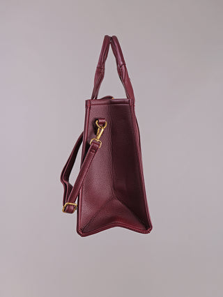 Regina Schrecker Shopper bordeaux in strukturiertem Leder mit verstärkten Henkeln, abnehmbarem Schulterriemen und goldfarbenen Beschlägen, zeigt eine markante dreieckige Seitenansicht.