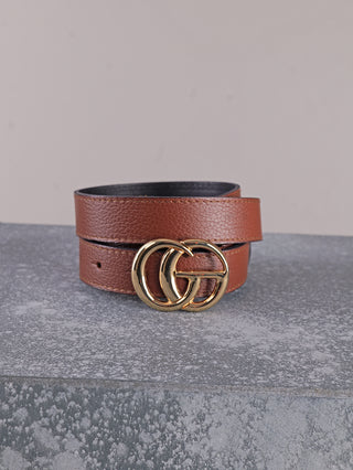 OFF#DLY Ledergürtel CG cognac aus braunem Leder mit einer goldfarbenen Schließe aus zwei ineinandergreifenden Ringen, auf einer grauen Steinoberfläche gerollt dargestellt.