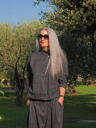 Die OFF#DLY Jacke Adira grey/red zeigt eine elegante, kastige Silhouette mit Stehkragen und dezentem Karomuster, getragen von einer reifen Frau in einem Garten, die Hände in den Taschen.