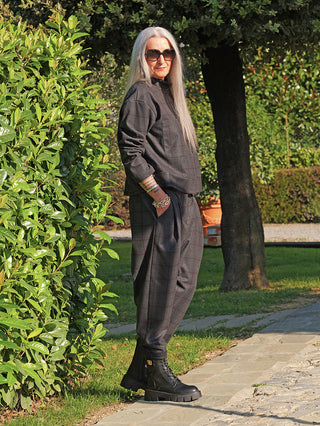 Person trägt die OFF#DLY Jacke Adira grey/red mit Stehkragen und Karomuster, kombiniert mit passenden Hosen und schwarzen, klobigen Stiefeln, auf einem gepflasterten Weg.