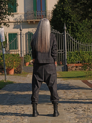 Person mit langen grauen Haaren trägt OFF#DLY Jacke Adira; lockerer, moderner Schnitt mit Stehkragen und dezentem Karomuster. Sie steht vor einem schmiedeeisernen Tor in urbaner Umgebung.