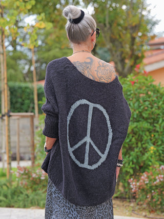 Person von hinten im Garten mit dem OFF#DLY Pulli Selma black, dessen lässiger, weiter Schnitt und großes Peace-Zeichen am Rücken sichtbar sind, trägt den Pullover off-shoulder.