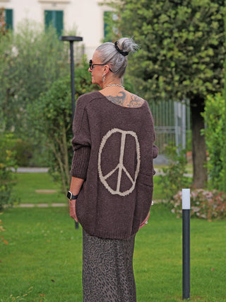 Person von hinten im Garten, trägt den OFF#DLY Pulli Selma braun mit weitem Schnitt und Peace-Zeichen auf dem Rücken, kombiniert mit einem fließenden animal-print Rock und Sonnenbrille.