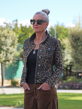 Frau im Garten trägt die OFF#DLY Denim Jacket Leonie black/camel, eine figurbetonte Jeansjacke mit Leo-Print über schwarzem Top, kombiniert mit braunen Cordhosen und auffälligen Accessoires.