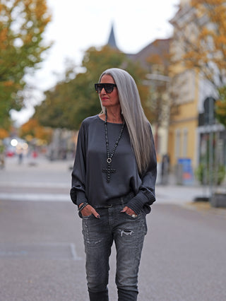 Frau trägt das OFF#DLY LS Shirt Valentina anthrazit mit weiten Ärmeln, locker fallend und elegant, auf einer herbstlichen Straße, kombiniert mit Sonnenbrille und grauer Jeans.