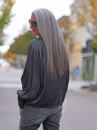 Person trägt das OFF#DLY LS Shirt Valentina anthrazit mit weiten, fließenden Ärmeln, während sie auf einer ruhigen Stadtstraße steht und über die Schulter blickt.