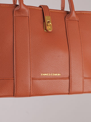 Nahaufnahme der Enrico Coveri Tote Bag cognac aus strukturiertem, genarbtem Leder, mit schmalen Schulterriemen und goldfarbenem Drehverschluss, goldener Schriftzug ENRICO COVERI auf der Vorderseite.