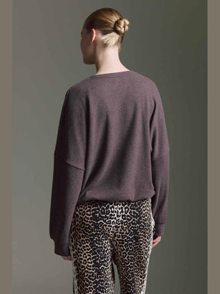Person von hinten in lockerem Cotton Candy Obdulia Tee espresso mit weitem V-Ausschnitt und Rollkanten, kombiniert mit eng anliegenden Leopardenmuster-Hosen, das Haar in einem tiefen Dutt gebunden.