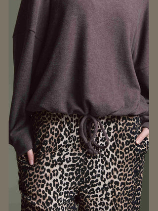 Die Cotton Candy Obdulia Tee espresso zeigt sich als locker geschnittenes, langärmeliges Shirt mit Bindeband am Saum, getragen über lässigen Leopardenmuster-Hosen, Hände in den Taschen.