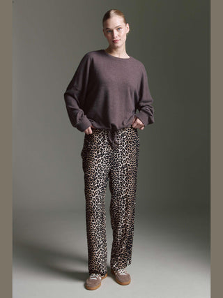 Frau trägt das Cotton Candy Obdulia Tee espresso, ein locker geschnittenes Longsleeve mit rundem Halsausschnitt und Bindeband am Saum, kombiniert mit weiten Leopardenmuster-Hosen und taupefarbenen Sneakers.