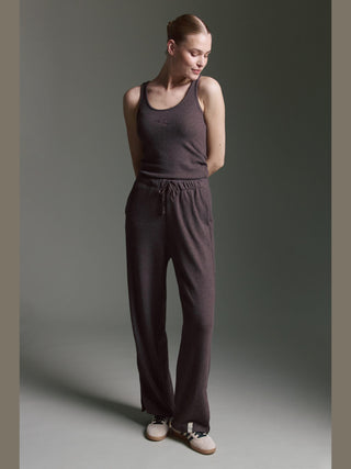 Eine junge Frau trägt das Cotton Candy Roca Top espresso, ein weiches, lässiges Langarmshirt mit V-Ausschnitt. Es ist in eine dunkle Loungehose gesteckt, die einen entspannten Look vervollständigt.