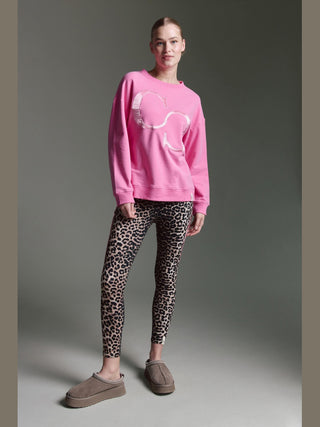 Person trägt das Cotton Candy. Sweat Lune pink, ein lockeres, bubblegum-pinkes Sweatshirt mit leicht distressiertem Grafik-Design, kombiniert mit leopardengemusterten Leggings und taupefarbenen, plüschgefütterten Slip-On-Schuhen.