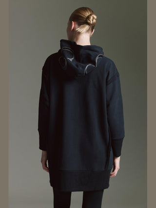 Person von hinten in einem oversized schwarzen Hoodie, dem Cotton Candy Sweat Luna black, mit Kapuze und kontrastierenden Nähten, kombiniert mit schmalen schwarzen Hosen. Haare zu einem ordentlichen Dutt gebunden.