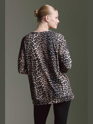 Frau mit lockerem Pferdeschwanz trägt ein Cotton Candy Tee Irma multicolor, ein locker sitzendes, langärmliges Oberteil mit Leopardenmuster und weitem V-Ausschnitt, kombiniert mit schwarzen Leggings.