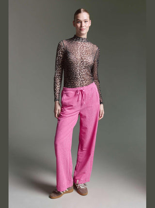 Frau in Cotton Candy Floortje Tee multicolor mit braun-schwarzem Leopardenmuster, kombiniert mit pinken Cordhosen und braunen Wildlederschuhen. Sie steht entspannt und selbstbewusst vor neutralem Hintergrund.