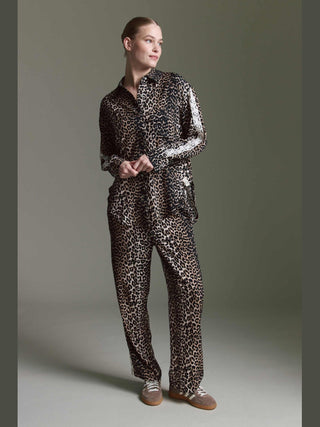 Person in einem Leopardenmuster-Ensemble, bestehend aus Bluse Olivia II multicolor und Hose, trägt Sneakers. Die Bluse hat einen lässigen Schnitt und ist aus 100% Viskose gefertigt.