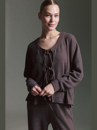 Eine junge Frau trägt den Cotton Candy Cardigan Odilie espresso, ein tiefbraunes Strickset mit offenem Vorderteil und Bindebändern, kombiniert mit entspannten Jogger-Hosen, vor neutralem Hintergrund.