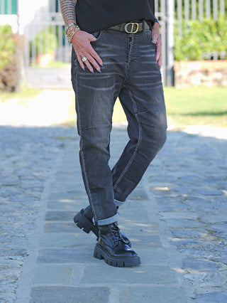 Person trägt die OFF#DLY Denim Mira Black Wash mit umgeschlagenen Säumen, kombiniert mit schwarzen Lederstiefeln und einem schwarzen Gürtel mit silberner Schnalle. Sichtbare Accessoires sind goldene und silberne Ringe.