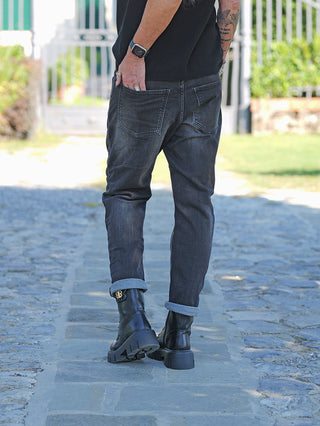 Die OFF#DLY Denim Mira Black Wash zeigt einen lässigen Schnitt mit umgeschlagenem Saum, getragen mit schwarzen Lederstiefeln, ergänzt durch Accessoires wie Ringe und eine Smartwatch.