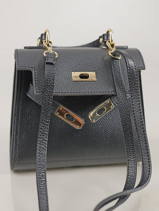 OFF#DLY Leder Bag black: Kleine schwarze Ledertasche mit goldfarbenen Beschlägen und langem Schulterriemen, offene Klappe mit dekorativen Schlossplatten, präsentiert vor neutralem Hintergrund.