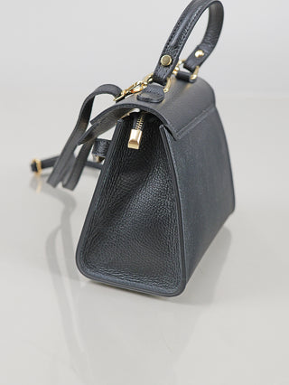 Kompakte, strukturierte OFF#DLY Leder Bag black mit goldfarbenen Beschlägen und einem oberen Tragegriff, auf einer glatten, hellen Oberfläche präsentiert, mit Reißverschluss und eleganten Befestigungen.