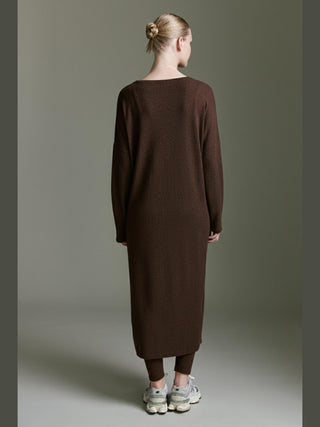 Frau von hinten in Cotton Candy Odith Dress espresso, locker geschnittenes, langes Kleid mit weitem Rundhalsausschnitt und seitlichem Schlitz, kombiniert mit dunklen Leggings und klobigen, hellgrauen Sneakers.