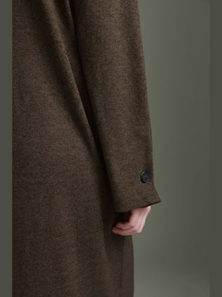 Nahaufnahme eines Arms in einem braunen Mantelärmel, der Teil des Cotton Candy Odith Dress espresso ist, mit dekorativem Knopfdetail am Ärmel, vor einem dezenten Hintergrund.