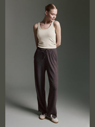 Frau trägt Cotton Candy Roca Top offwhite, ein ärmelloses, beige Tanktop mit Rundhalsausschnitt, kombiniert mit grauen Lounge-Hosen. Das Top hat breite Träger und ein dezentes Logo auf der Brust.