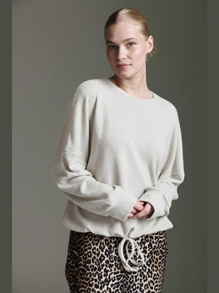 Junge Frau trägt Cotton Candy Obdulia Tee offwhite, ein locker geschnittenes Longsleeve mit rundem Halsausschnitt und Bindeband am Saum, kombiniert mit einem Leopardenmuster-Rock oder -Hose.