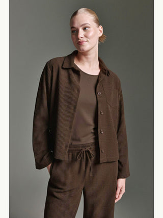 Die Frau trägt die Cotton Candy Bluse Jacke espresso, eine locker geschnittene Cordjacke mit Knopfleiste, über einem passenden Tanktop und Hose, ideal für entspannte Freizeitlooks.