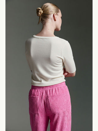 Person von hinten mit eng anliegendem Cotton Candy Tee Bale in Offwhite, das kurze Ärmel und einen Rundhalsausschnitt hat, kombiniert mit auffälligen, strukturierten pinken Hosen mit elastischem Bund und Taschen.