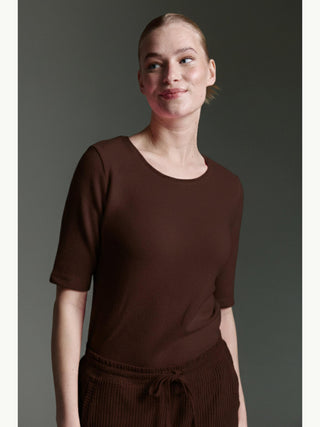 Frau trägt das Cotton Candy Tee Bale espresso, ein kurzärmeliges, dunkelbraunes Oberteil, leicht zur Seite gedreht, mit einem dezenten Lächeln, passend zu einer gleichfarbigen Strickhose.