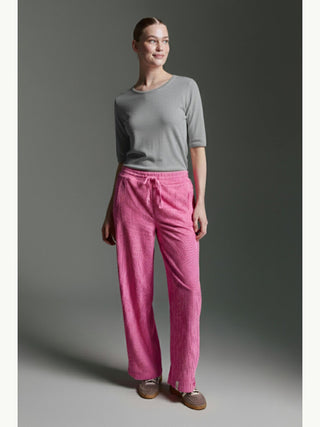 Frau trägt das Cotton Candy Tee Bale grey melange, ein graues, halblanges Shirt mit Rundhalsausschnitt, kombiniert mit leuchtend pinken, lockeren Hosen und lässigen Slip-On-Schuhen vor neutralem Hintergrund.