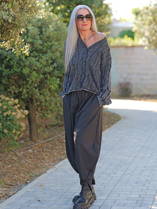 Ältere Frau trägt OFF#DLY West Ada black wash, eine lockere graue Strickweste mit markantem Muster und V-Ausschnitt, kombiniert mit weiten schwarzen Haremshosen und klobigen Platform-Boots.