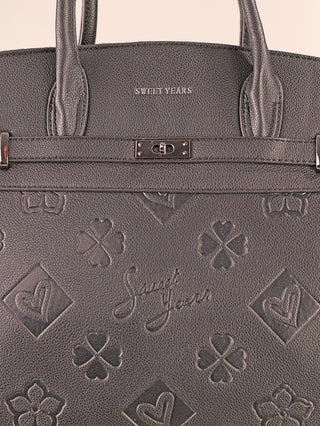 Nahaufnahme der Sweet Years Logo Bag black, einer schwarzen Henkeltasche aus Polyurethan mit Herz- und Kleeblatt-Prägung, langen Griffen und Metallverschluss. Markenname auf Vorderseite geprägt und oben gedruckt.