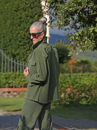 Person im Freien trägt ein oversized OFF#DLY Cord Hemd Violetta grün mit lässigem Schnitt und offenen Saumkanten, kombiniert mit passender Hose und dunkler Sonnenbrille.