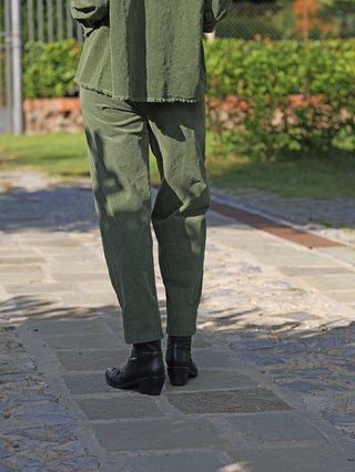 Die OFF#DLY Cord Pant Veronica grün zeigt sich im lässigen, lockeren Schnitt, getragen mit schwarzen Lederstiefeletten auf einem Gartenweg.